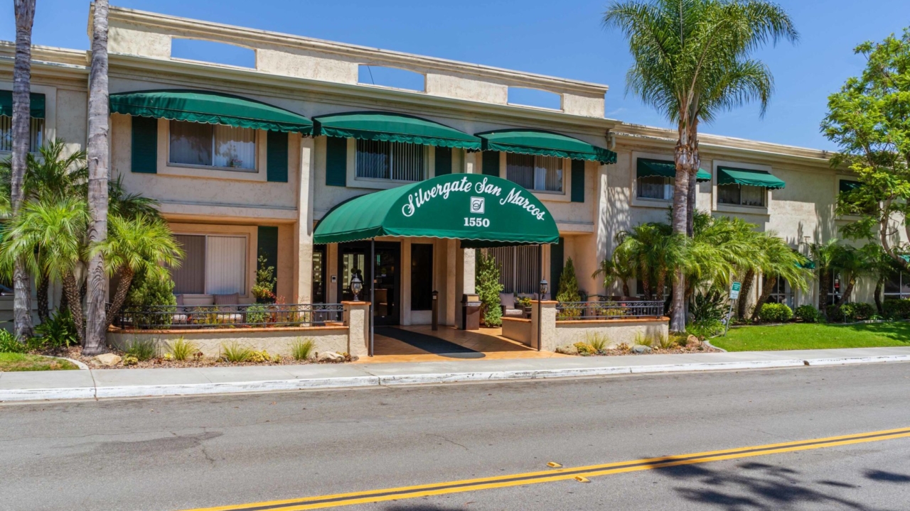 Silvergate San Marcos' exterior has several green awnings. Several green palm trees adorn the lawn.
